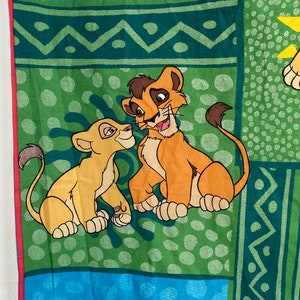 Puede incluir: Una tela verde, azul y amarilla con un diseño de patchwork que presenta imágenes de dibujos animados de Simba y Nala de El Rey León de Disney.