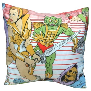 May include: Square pillow featuring a colorful cartoon illustration of action figures. The design includes a female warrior in gold armor, a green monster with a sword, and other characters on a white background with red stripes. The pillow is a decorative item.