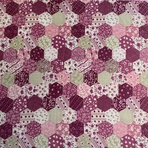 May include: A fabric with a repeating pattern of hexagonal shapes. The hexagons feature various floral, paisley, and geometric designs in shades of pink, burgundy, and cream. The fabric is suitable for quilting or crafting projects.