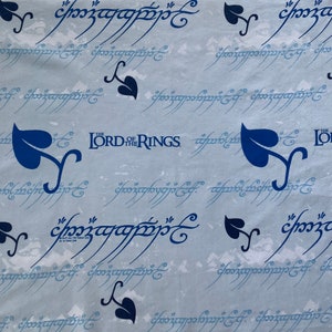 May include: Blue and white fabric with a repeating pattern of the words "The Lord of the Rings" and a stylised script. The script is in a blue colour and the words are in a darker blue colour. There are also small blue leaf designs throughout the fabric.
