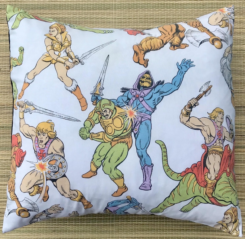 May include: White square pillow featuring a colorful action-packed illustration of various characters in a comic book style. The design includes figures with swords, shields, and other weapons, with a retro cartoon aesthetic.