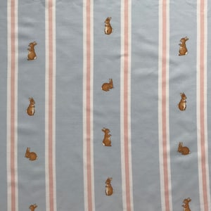 Puede incluir: Tela a rayas azules y rosas con un patrón repetido de conejos marrones.