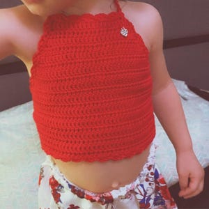 Puede incluir: Top halter de ganchillo rojo brillante, hecho a mano, con borde festoneado. El top presenta un pequeño adorno decorativo cerca del escote. El top se combina con una parte inferior con estampado floral.
