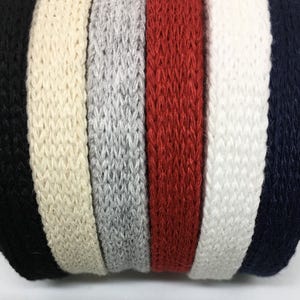 May include: A close-up of six different colored knitted cotton webbing straps. The straps are black, beige, gray, red, white, and navy blue.