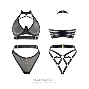 Puede incluir: Un conjunto de lencería y arneses negros. El conjunto incluye un top halter, un sujetador con tirantes, un tanga y un arnés. Todas las piezas presentan herrajes dorados y están hechas de tela negra transparente. La marca "MARI MOTH" está impresa en la parte inferior.