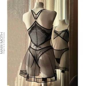 Könnte beinhalten: Schwarzes Dessous-Set auf einer Schaufensterpuppe, bestehend aus einem transparenten Babydoll-Kleid mit gepunktetem Rock und einem passenden String. Das Set hat eine Spitze am Oberteil und Trägern. Der Markenname "MARI MOTH lingerie & harnesses" ist sichtbar.
