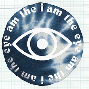 May include: A circular, tie-dye design in shades of blue and white, featuring a white eye graphic in the center. The text "eye am the i am the eye" is printed in a white, stylized font around the eye.
