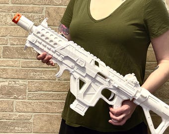 May include: A white toy rifle featuring a futuristic design with a prominent orange tip on the barrel. The prop includes a textured handguard, a central magazine well, a trigger assembly, and a skeletonized stock, all rendered in a matte white finish.