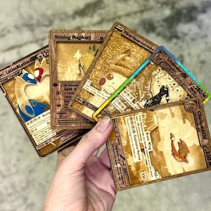 以下が含まれることがあります： ラティアス＆ラティオス、ピカチュウ、リザードンなどのキャラクターが描かれた木製のポケモンカードのコレクション。 カードは、金色のアクセントとテキストが施された詳細な彫刻デザインです。 カードは手で持たれています。