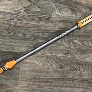 May include: A silver and brown decorative staff with a twisted metal shaft and a leather handle. The handle is decorated with a black and white pattern and a gold tassel.