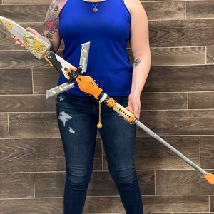 May include: A silver and orange spear with a decorative design. The spear has a long, thin shaft and a sharp point. The spear is held by a person wearing blue jeans.