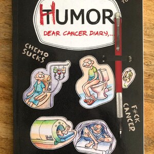 Op de afbeelding: Een zwart boek getiteld Humor Dear Cancer Diary door Federico Muelas met een bevestigd rood vulpotlood. De kaft bevat cartoonillustraties van medische behandelingen en de tekst Humor Beats Tumor, Chemo Sucks en Cancer F*ck.