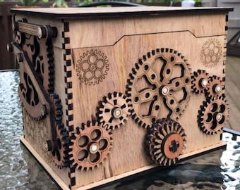Op de afbeelding: Een houten doos met een decoratief ontwerp van tandwielen en tandwielen. De doos is gemaakt van lichtbruin hout en heeft een zwarte rand.
