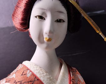 Japanese Geisha doll, bisque hand painted face, hands, foot. Elaborately dressed, on platform