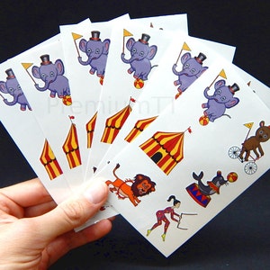 Puede incluir: Un conjunto de ocho tatuajes temporales coloridos con animales de circo, incluyendo un elefante, un león, un oso y una foca. Los tatuajes también incluyen una carpa de circo y un monociclo.