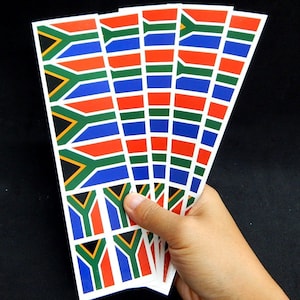 Könnte beinhalten: Ein Satz mit sechs Aufklebern der südafrikanischen Flagge. Die Aufkleber sind auf weißem Papier gedruckt und zeigen die Farben der südafrikanischen Flagge: Grün, Gelb, Rot, Schwarz und Blau.