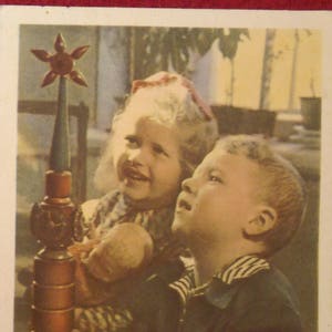 Puede incluir: Fotografía vintage de dos niños mirando hacia arriba a un juguete de madera con una estrella en la parte superior. El juguete es marrón y tiene un diseño decorativo. Los niños llevan ropa vintage.