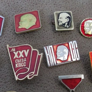 Può includere: Una collezione di dieci spille smaltate vintage raffiguranti l'immagine di un uomo con la barba. Le spille sono di colore rosso, bianco e oro e presentano vari disegni, tra cui una falce e un martello, una stella e uno stendardo con il testo "XXV съезд КПСС".