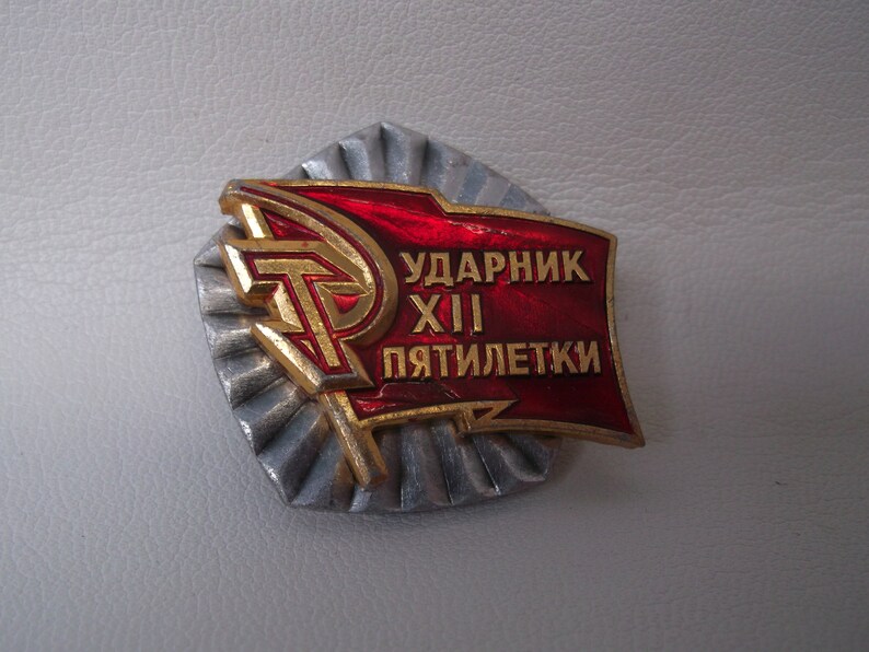 May include: A red and gold metal badge with the text "Ударник XIII пятилетки" which translates to "Shock Worker of the 13th Five-Year Plan".