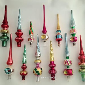 May include: A collection of twelve vintage glass Christmas tree toppers in various shapes and colours, including red, green, gold, silver, and pink. Each topper features a long, pointed spire and a decorative base with reflective finishes.