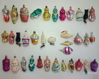 May include: A collection of vintage glass Christmas ornaments in various shapes including animals, birds, fish, and figures. The ornaments feature diverse colors like pink, gold, green, silver, and black, with some displaying painted details.