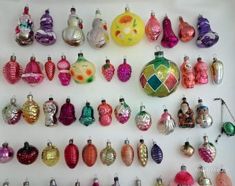 May include: A collection of vintage glass Christmas ornaments in various shapes, including spheres, bells, fruits, and figures. The ornaments feature diverse colors like red, gold, green, purple, and pink, with some displaying painted details and textures.