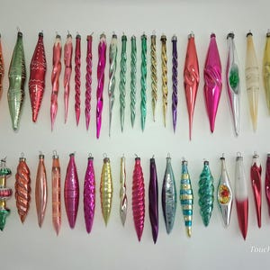 May include: A collection of forty-eight vintage glass Christmas tree ornaments in various elongated shapes, including icicles, spirals, and teardrops. The ornaments feature a vibrant array of metallic and glossy colors, including red, green, gold, pink, purple, silver, and orange. The text TouchTheOld is visible in the bottom right corner.