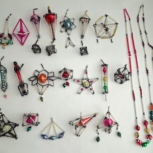 May include: A collection of vintage geometric Christmas ornaments and two long beaded garlands. The ornaments feature metallic glass spheres and beads encased in dark wire frames, including star, diamond, and lantern shapes in red, blue, and gold.