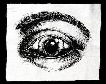 May include: A black and white illustration of a human eye on a white fabric background.
