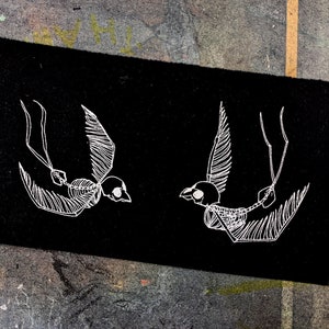 Może przedstawiać: Dwie białe sylwetki szkieletowych ptaków na czarnym tle. Ptaki patrzą na siebie z rozpostartymi skrzydłami.