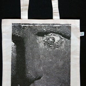 Könnte beinhalten: Weiße Canvas-Tragetasche mit einem schwarz-weißen Grafikdruck eines Auges. Die Tasche hat zwei weiße Henkel.
