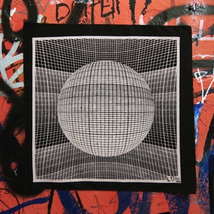 May include: A square black fabric patch featuring a white screen-printed graphic of a three-dimensional sphere centered within a distorted grid pattern. The bottom right corner includes the text LYSERGIC BERLIN printed in a simple sans-serif font.