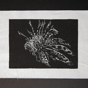 Könnte beinhalten: Ein Schwarz-Weiß-Linolschnitt eines Feuerfisches auf einem weißen Stoffhintergrund.
