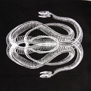 Puede incluir: Textil negro con una ilustración blanca de un esqueleto de serpiente. La estructura esquelética de la serpiente es detallada, con la columna vertebral y las costillas visibles. El diseño es simétrico, con la forma de la serpiente reflejada.