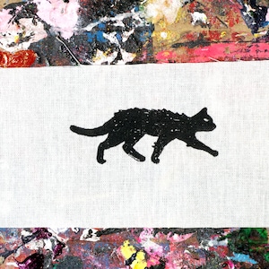 May include: A black cat silhouette printed on a white fabric patch. The patch is on a colorful background with paint splatters.