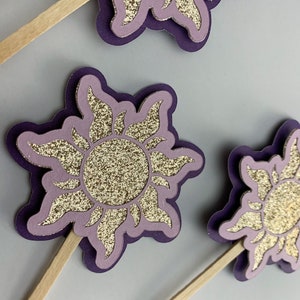 May include: Purple and gold glitter sun cupcake toppers with wooden sticks.