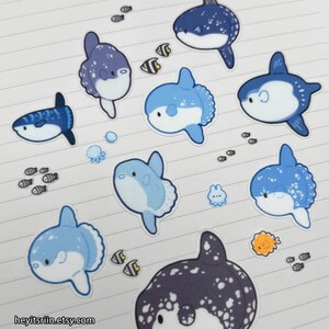 Peut inclure: Collection d'autocollants sur le th&egrave;me de l'oc&eacute;an, avec des poissons-lunes bleus et blancs, de petits poissons et d'autres cr&eacute;atures marines. Les autocollants sont dispos&eacute;s sur du papier lign&eacute;. Le nom de la boutique Etsy est visible.
