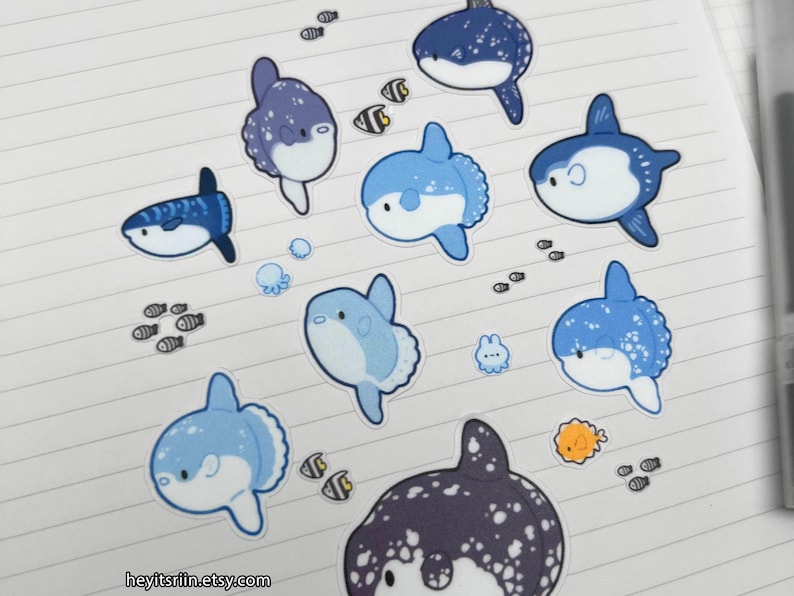 Peut inclure: Collection d'autocollants sur le th&egrave;me de l'oc&eacute;an, avec des poissons-lunes bleus et blancs, de petits poissons et d'autres cr&eacute;atures marines. Les autocollants sont dispos&eacute;s sur du papier lign&eacute;. Le nom de la boutique Etsy est visible.