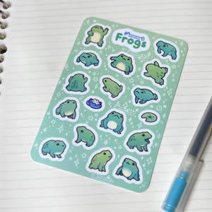 May include: A sheet of green frog stickers with white outlines. The stickers feature various poses of frogs with white stars and other designs in the background. The sheet says "Frogs" in a white banner at the top.