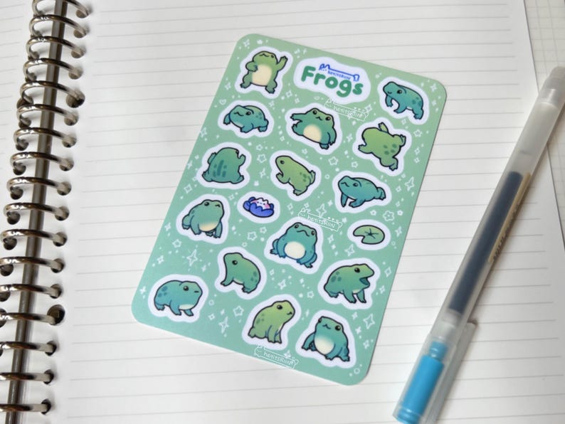 May include: A sheet of green frog stickers with white outlines. The stickers feature various poses of frogs with white stars and other designs in the background. The sheet says "Frogs" in a white banner at the top.