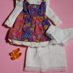 May include: A doll outfit set with a floral print dress, white lace-trimmed slip, white lace-trimmed underwear, and a pair of orange shoes.