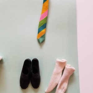 May include: A colorful striped tie in shades of green, orange, pink, and blue, paired with black shoes and white socks. The tie is knotted at the top. The items are arranged on a light blue and pink background.