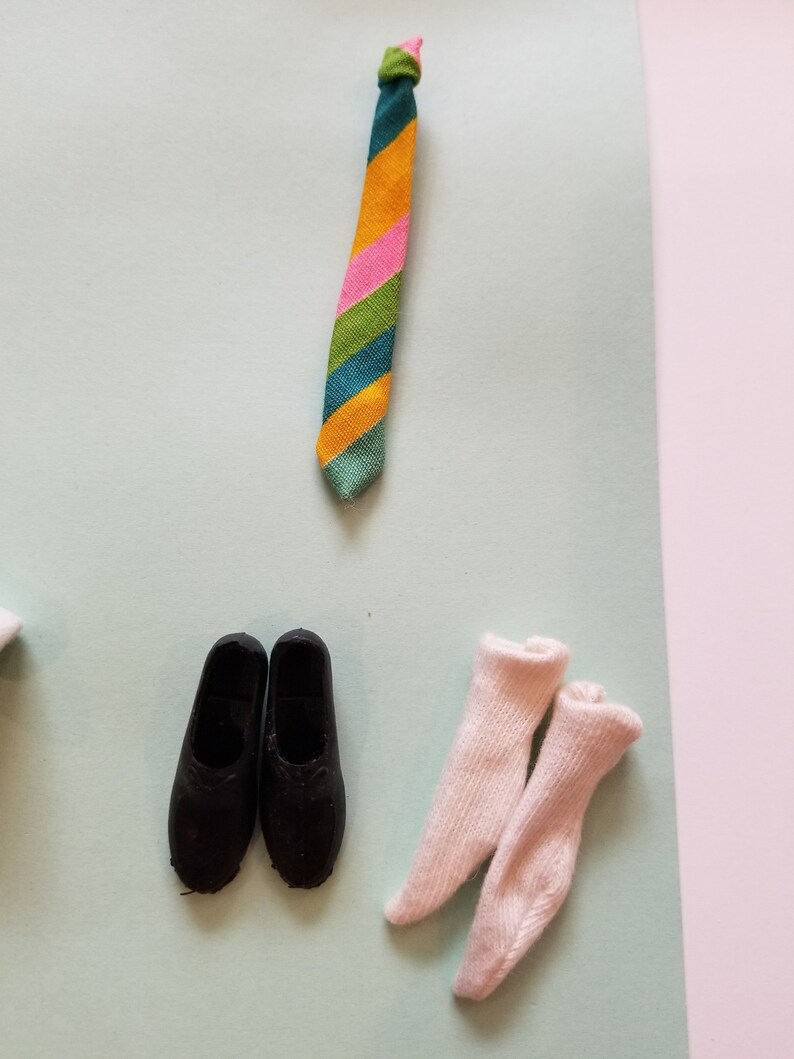 May include: A colorful striped tie in shades of green, orange, pink, and blue, paired with black shoes and white socks. The tie is knotted at the top. The items are arranged on a light blue and pink background.