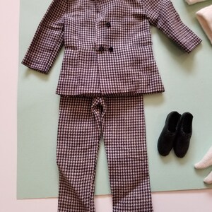 May include: A miniature houndstooth suit set, including a jacket with two black buttons and matching pants. The suit is paired with black shoes. The suit is in a black and white pattern.