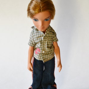 Könnte beinhalten: Eine Puppe mit braunen Haaren und blauen Augen, die ein kariertes Hemd und eine blaue Jeans trägt. Die Puppe steht auf einem weißen Hintergrund.