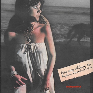 May include: Album cover featuring Linda Ronstadt in a white strapless dress, with the text "HASTEN DOWN THE WIND" and "Her new album on Asylum Records & Tapes." The image has a vintage aesthetic with a beach backdrop.