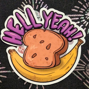 Pode incluir: Um autocolante com uma ilustração de desenho animado de uma fatia de torrada e uma banana, com as palavras "HELL YEAH!" em letras roxas. O autocolante tem uma borda branca e está sobre um fundo preto com desenhos de estrelas brilhantes.