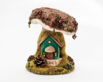 May include: A whimsical felt mushroom house with a green door and windows, decorated with beads and a butterfly. The mushroom is brown and white with a green base.