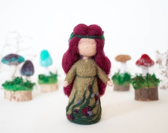 May include: A handmade felt doll with long, burgundy hair and a green dress adorned with floral details. The doll is surrounded by felted mushrooms of various colors, set on wooden bases, creating a whimsical forest scene.