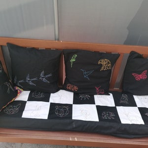 May include: A black bench with four black and white geometric patterned pillows. The pillows have colorful embroidery of animals and birds, including a butterfly, a hummingbird, a bird, and an eagle.